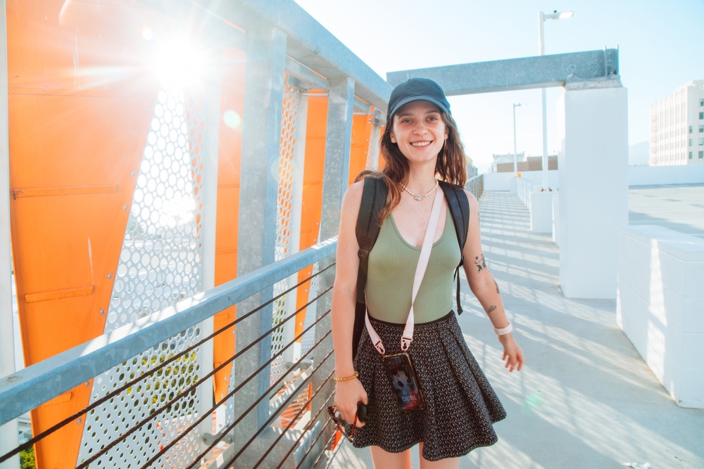 Cheerful young woman with a backpack on the modern pedestrian bridge. Student on the sunny streets of Santa Monica. California.