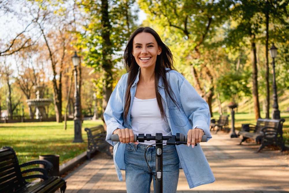 Close up of young happy fun woman wearing casual clothes riding e-scooter transport walking rest relax in spring green city park outdoors on nature. Urban lifestyle concept