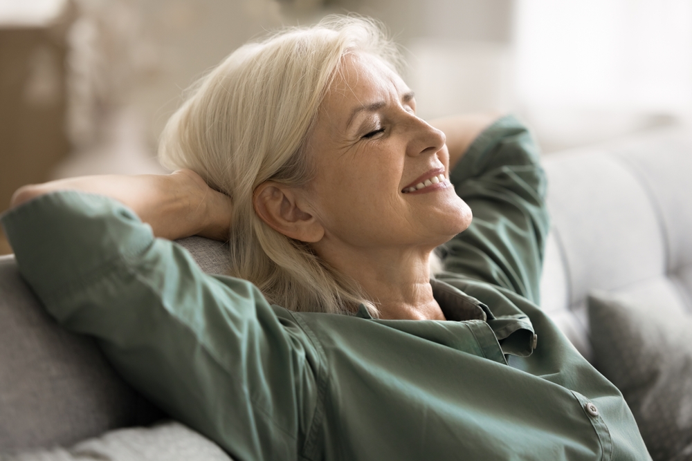 Emotional balance and inner peace. Carefree elderly woman pensioner recline on sofa in comfortable pose hands behind head dream with closed eyes breath fresh air relax at home alone. Close up portrait