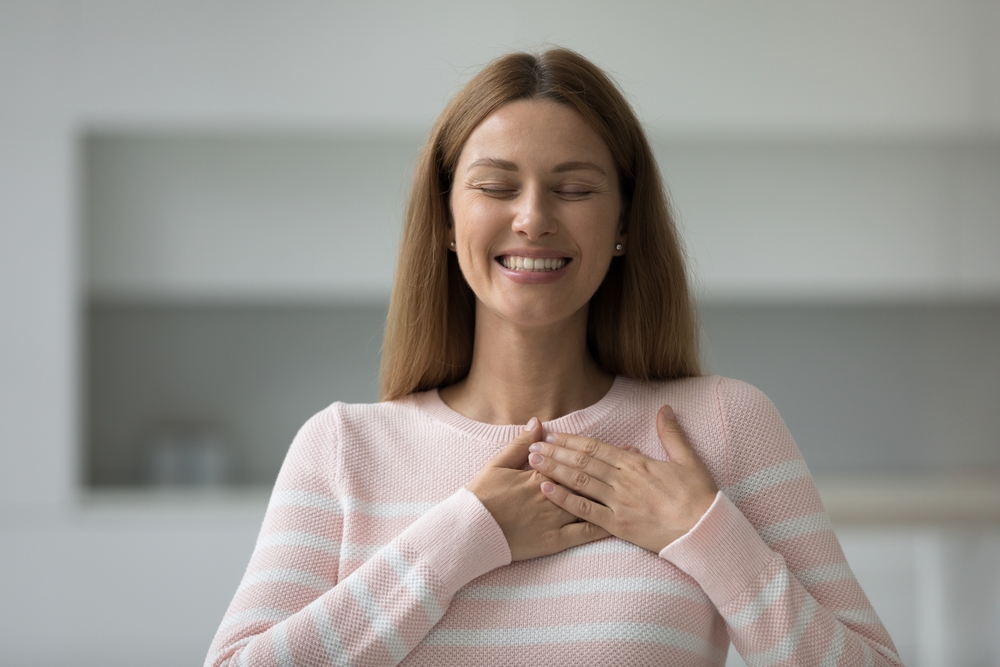 Headshot portrait young attractive woman holding folded palms on chest, close her eyes, express gratitude or praying, feels thankful, posing indoors, female volunteer showing kindness looking grateful