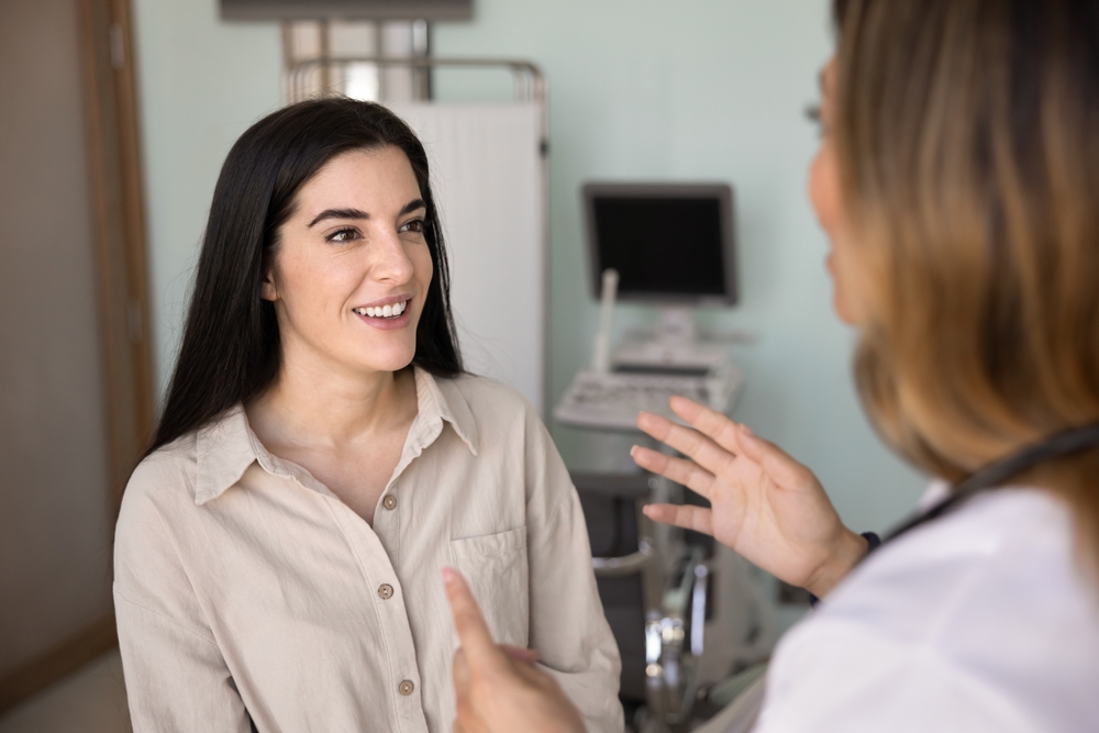 Positive young Latin patient woman talking to doctor in ultrasound diagnosis room, visiting clinic for checkup, meeting with healthcare professional specialist for consultation
