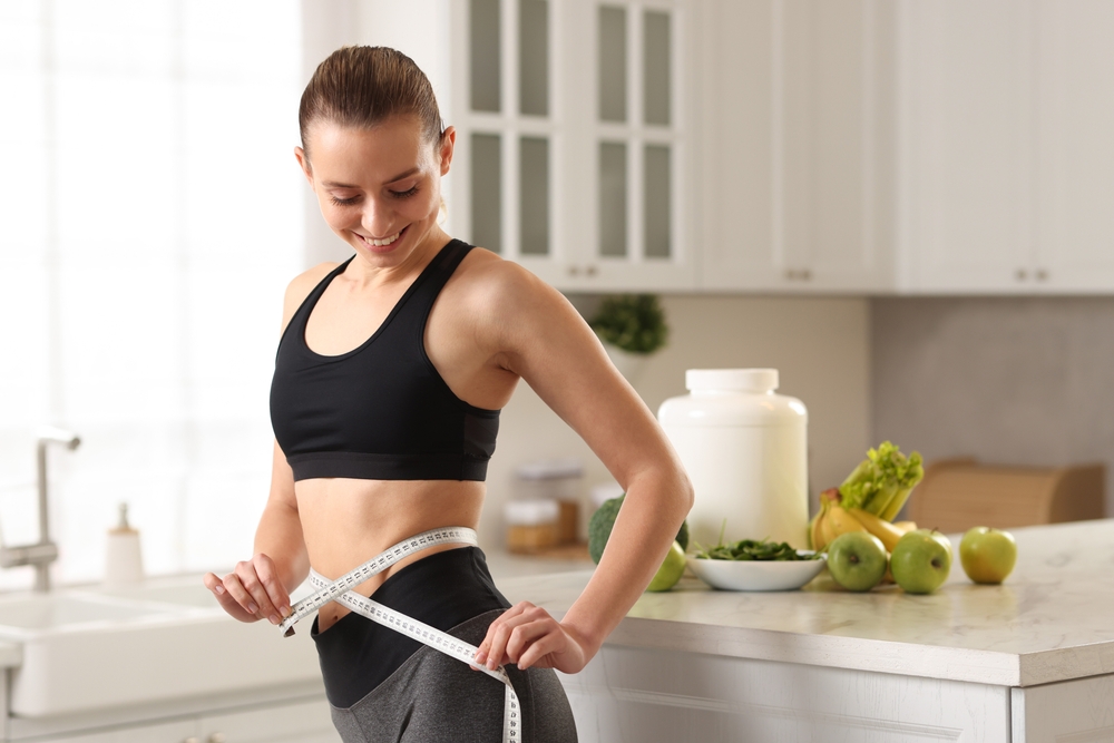 Weight loss. Woman measuring waist with tape in kitchen