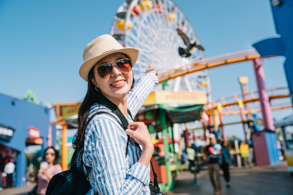 a joyful female traveler pointing to the Ferris wheel which she wants to try